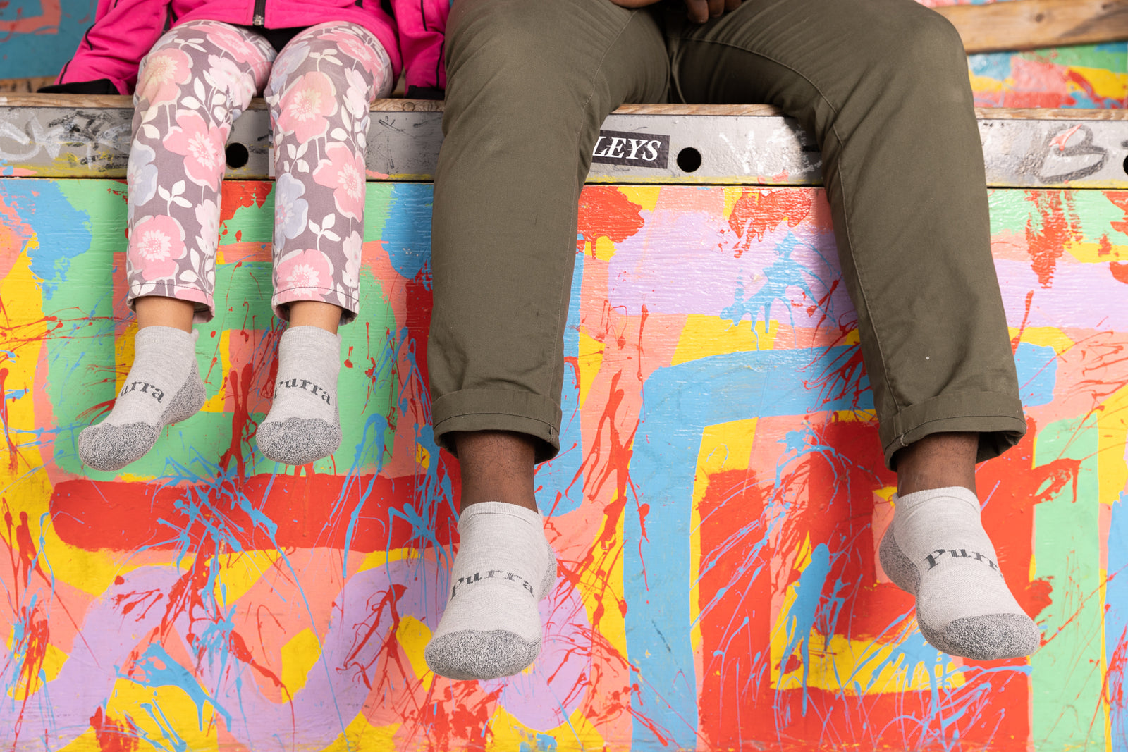 A quick rest for Dad and Daughter on a multi-colored painted concrete step.  The little girl is was wearing her Purra Light Grey No Show socks visible under her pink floral pants and the Dad is also wearing his antimicrobial Light Grey Purra No Show Socks.